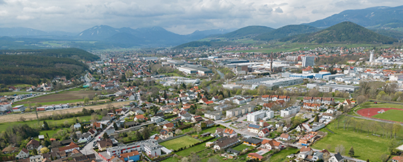 Ternitz Luftaufnahme von Ternitz mit Wohnhäusern, Industriegebäuden und Sportplatz, umgeben von grünen Hügeln und Bergen im Hintergrund.